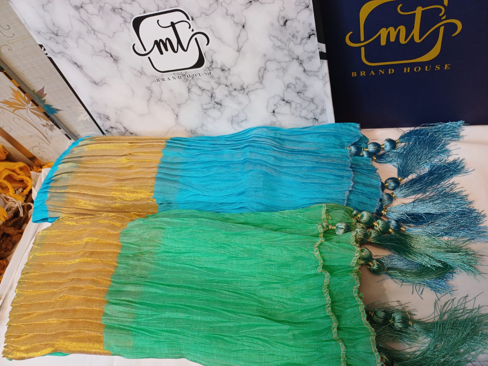 Colorful fabric with tassels on a marble surface, featuring the 'MT' brand logo.