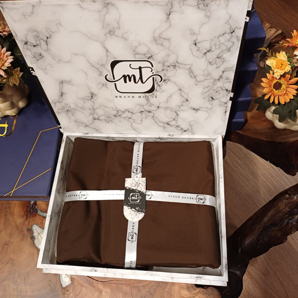 Open box with a brown item inside, featuring a marble-patterned lid with 'mt' branding, on a wooden surface with flowers.
