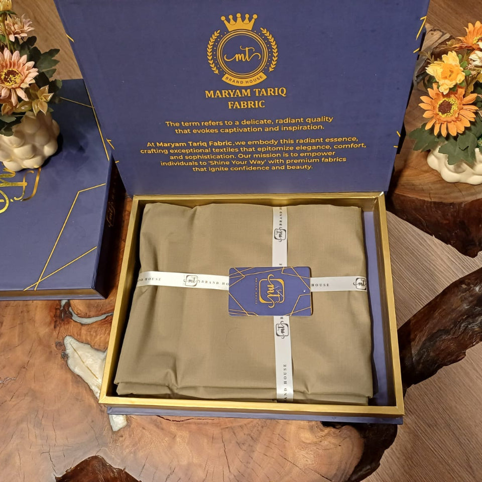 Brown fabric in a Maryam Tariq box on a wooden surface with decorative elements.