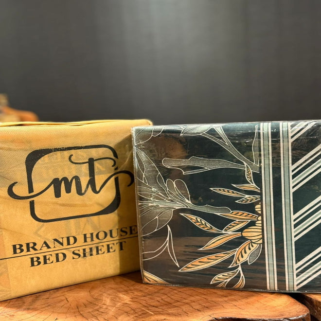 Box of brand house bed sheets with a decorative cover on a wooden surface.